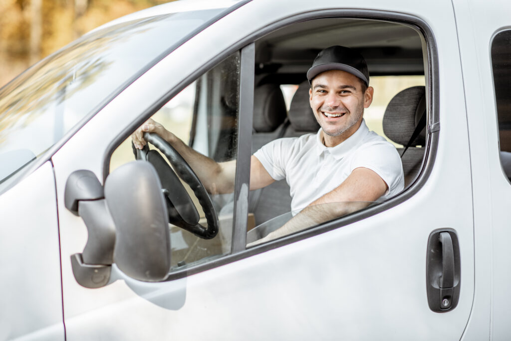 Autista sorridente al volante di un veicolo commerciale bianco, ideale per illustrare servizi di noleggio auto con conducente e la possibilità di aggiungere un guidatore autorizzato.